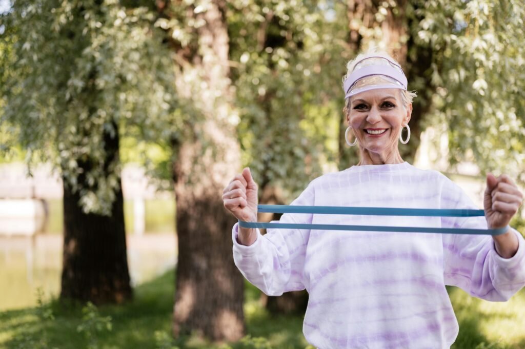 pexels-photo-8417525-8417525 A cheerful senior woman engaging in fitness with a resistance band outdoors in a park setting.